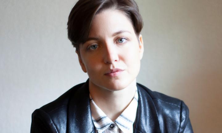 K Iver poet with short hair swooped to the side, wearing a collared striped shirt and black jacket