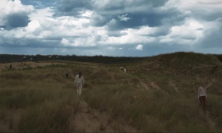 five people walking on dunes with overcast sky