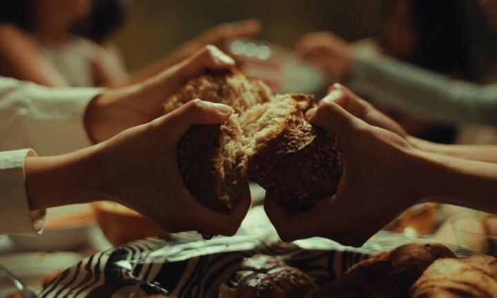 3 pairs of hands breaking bread over a fully laden table