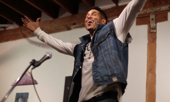 Eddie Goines performing his poem "Overcome" smiling with upraised arms