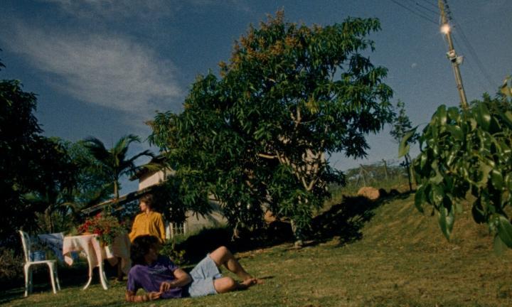 a young man reclines on grass and a woman looks to the left