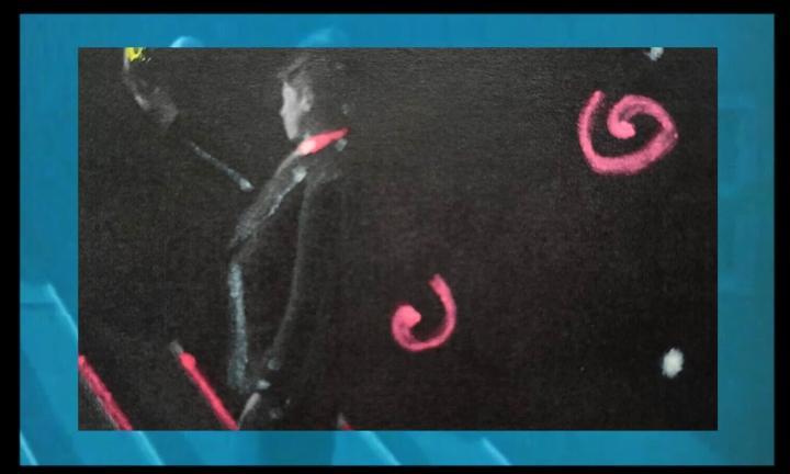 person in a tux with arm raised with a blue border around and pink spirals