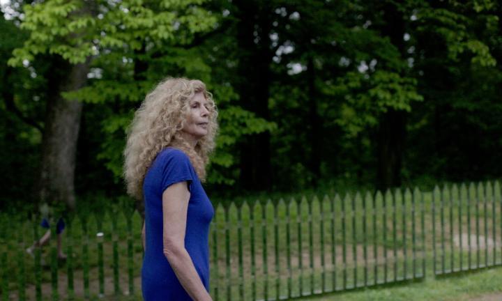 Poet Marie Howe walking outside next to mirrored picket fence 