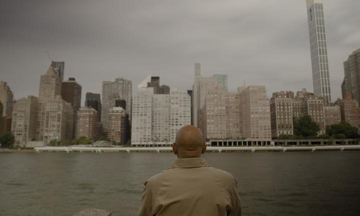 a bald man looking across a river at tall buildings