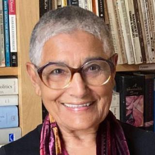 smiling woman with short cropped gray hair and round glasses in front of a bookshelf