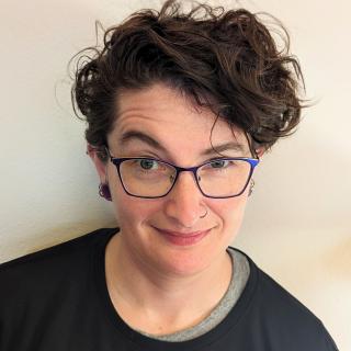Writer with blue frame glasses, nose ring, and cool wavy hair. 