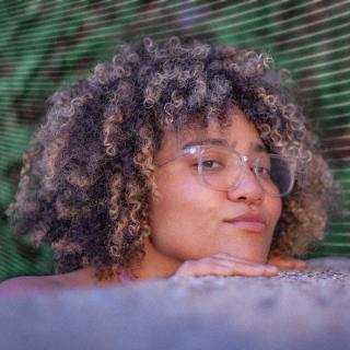 Sasha Debevec-McKenney, poet with curly hair and glasses peering over blurred object