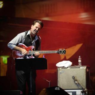 John McLean on stage playing electric guitar with amp in background