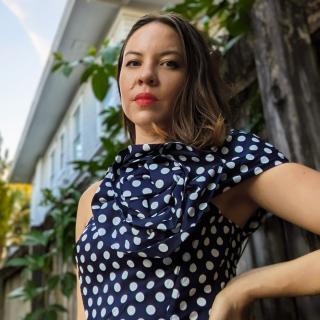 photo of author with hand on hip. house and plants in background.