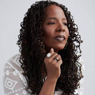 Donna Woodall looking right with long curly hair and a white gauzy shirt with geometric patterns
